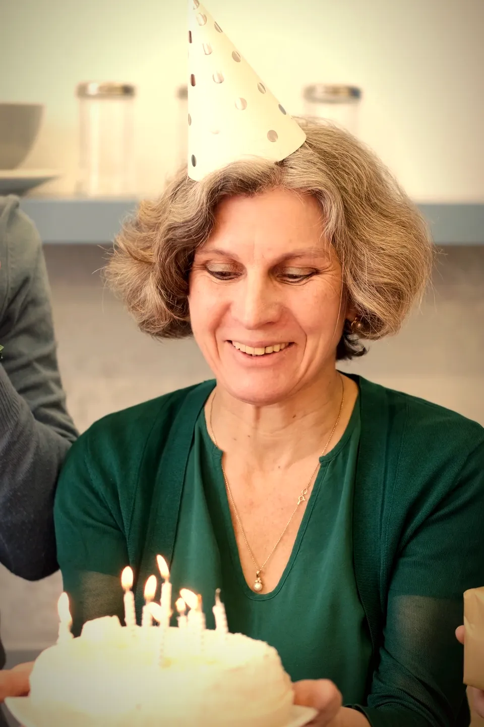 Una mujer con gorrito de cumpleaños sostiene una torta con velas encendidas.